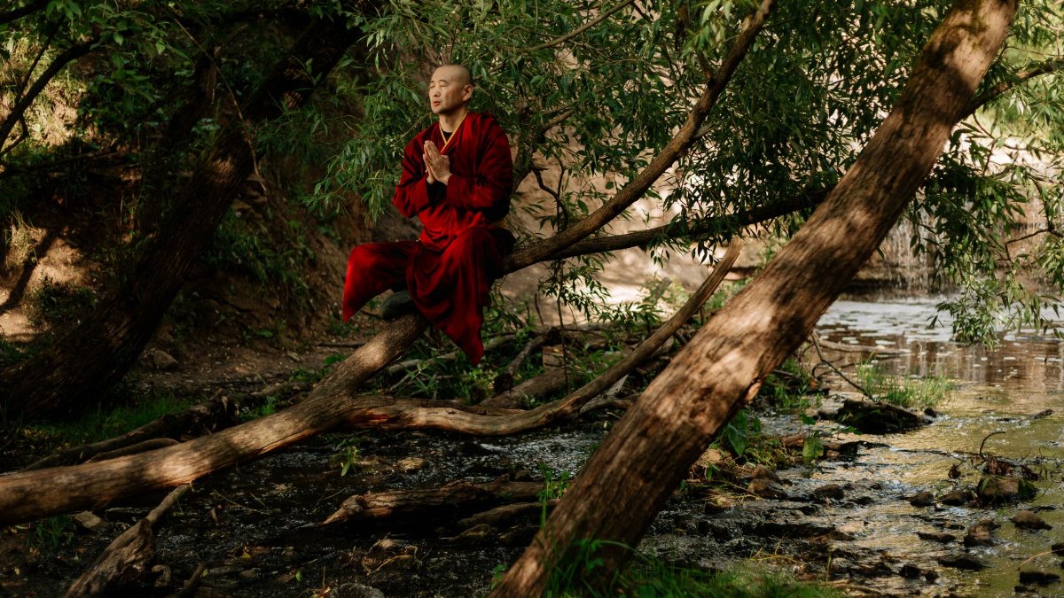 A serene monk in red robes meditates by a forest stream, embracing nature's tranquility.