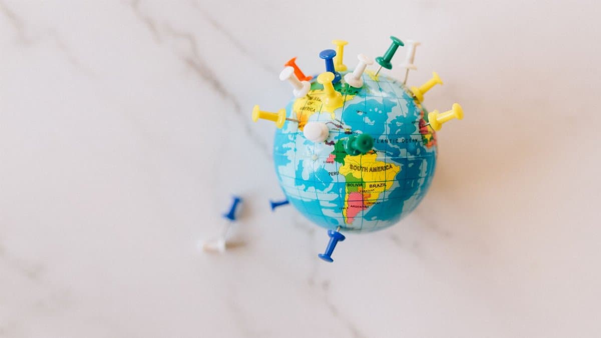 A globe decorated with colorful push pins on a marble surface represents global connections
