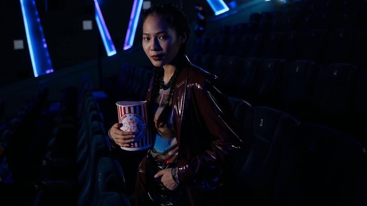 A stylish young woman holding popcorn in a dimly lit cinema, ready for a movie night experience.