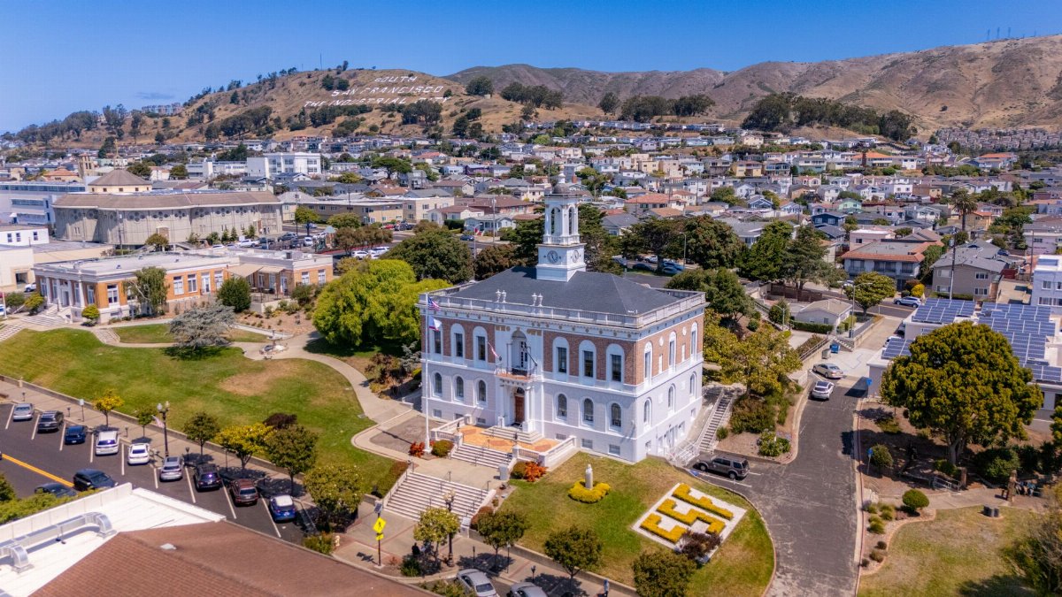 Stunning aerial view of a historic building and cityscape in South San Francisco under clear blue skies.