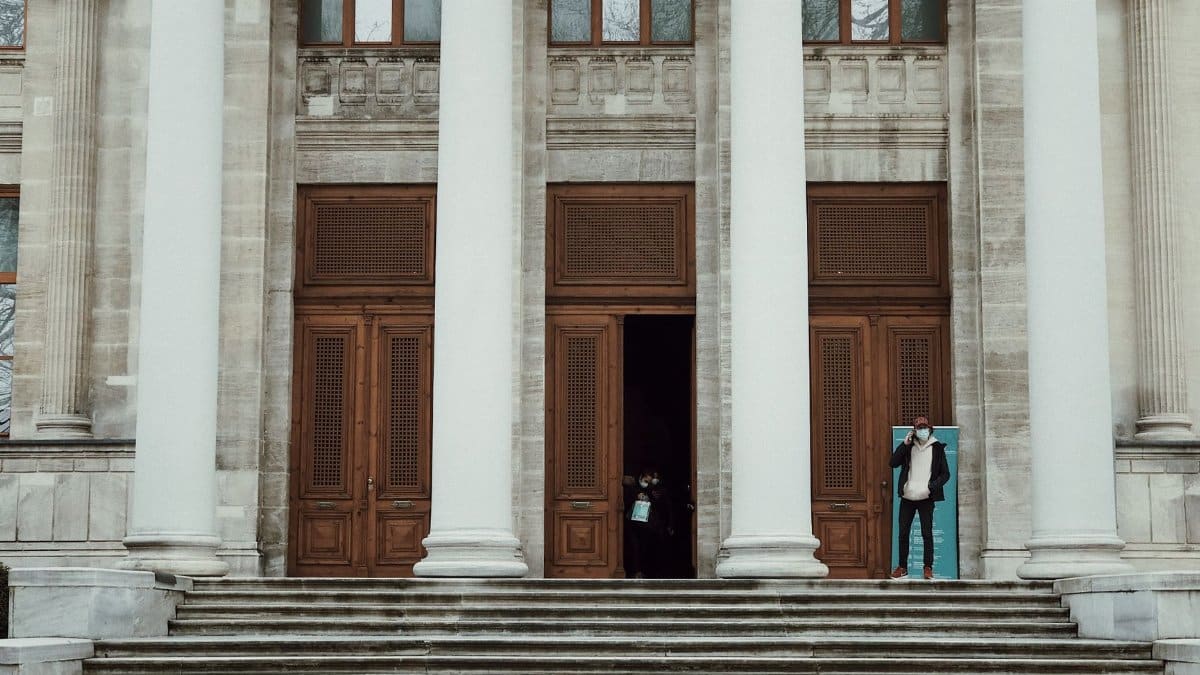 Exterior view of a neoclassical building with large columns and a staircase, featuring a person entering.