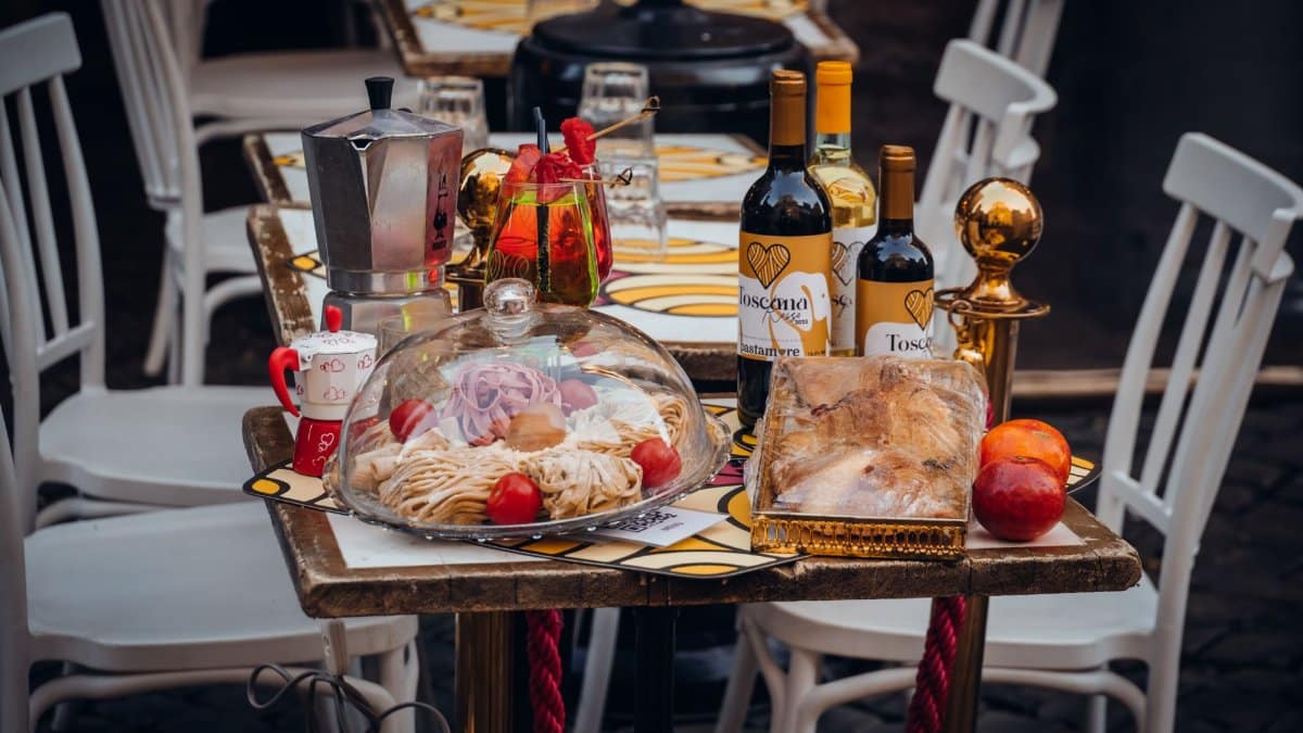 Close-up of a dining table set outdoors with Italian cuisine, featuring wine, coffee pot, and pastries.