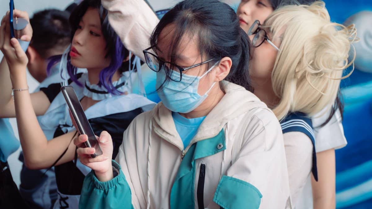 Group of young cosplayers using smartphones at an event, dressed in various costumes.
