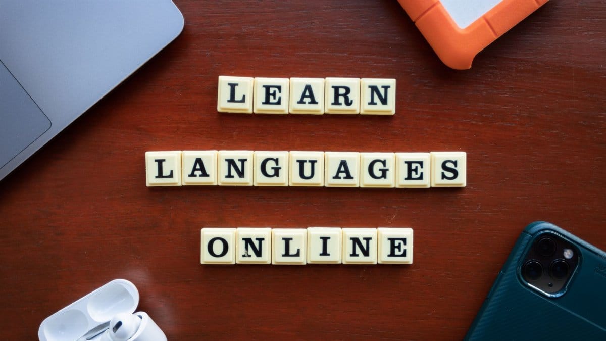 Flat lay of language learning tools with devices and text blocks on desk.