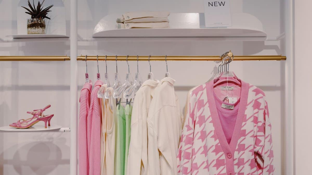 Stylish women's clothing on rack featuring pink cardigan and green dress inside a boutique.