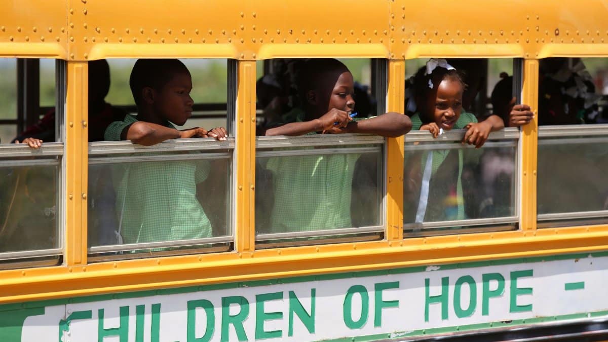 Children peering out of a yellow school bus in Dominicus, expressing hope and curiosity.