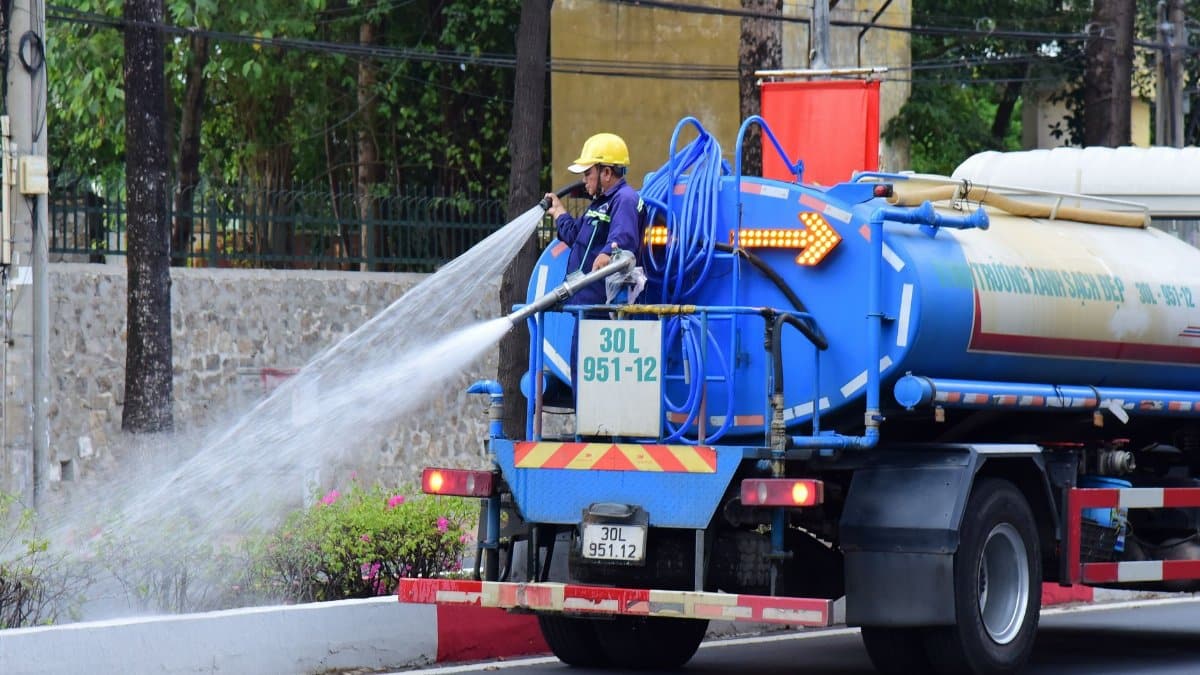 A worker operates a water truck cleaning a city street, ensuring urban cleanliness.