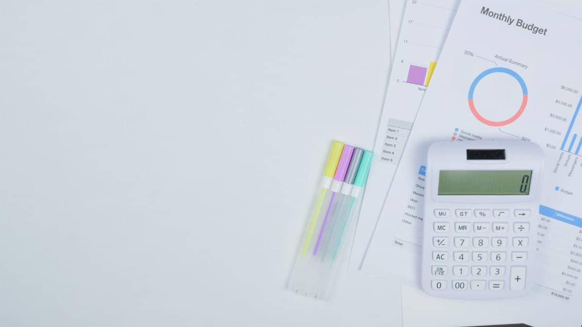 Minimalist office desk with a calculator, budget planning documents, and colorful pens.