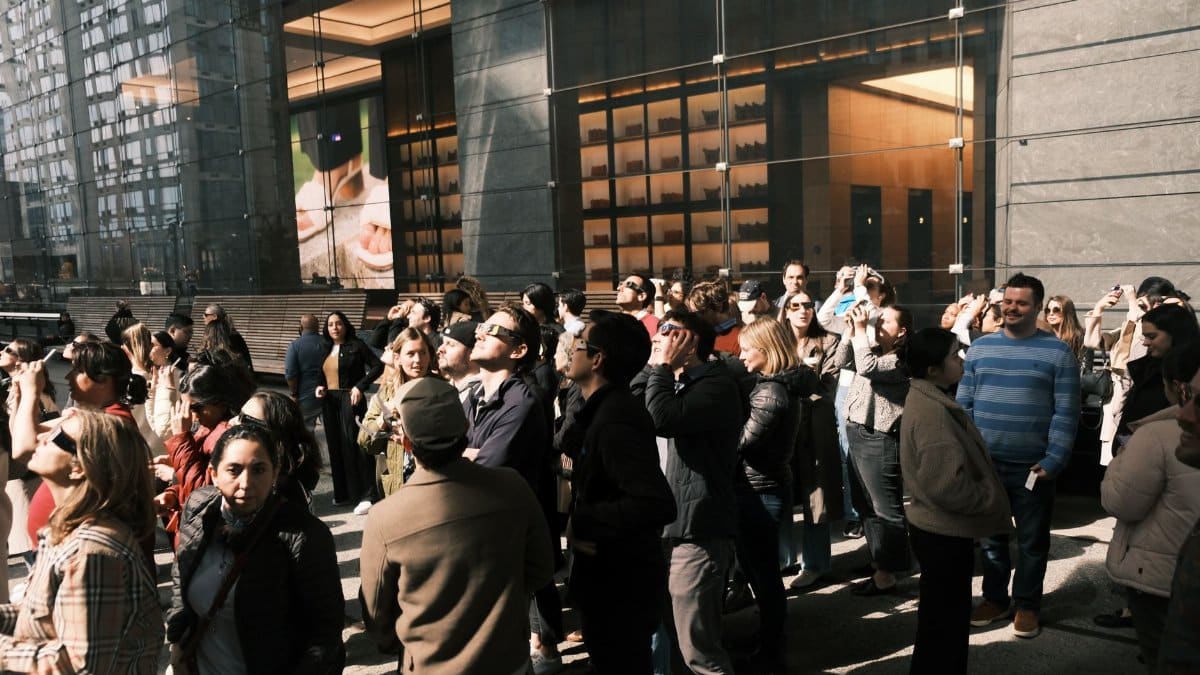 People gathered outside a glass-walled modern building during the day, observing an event.
