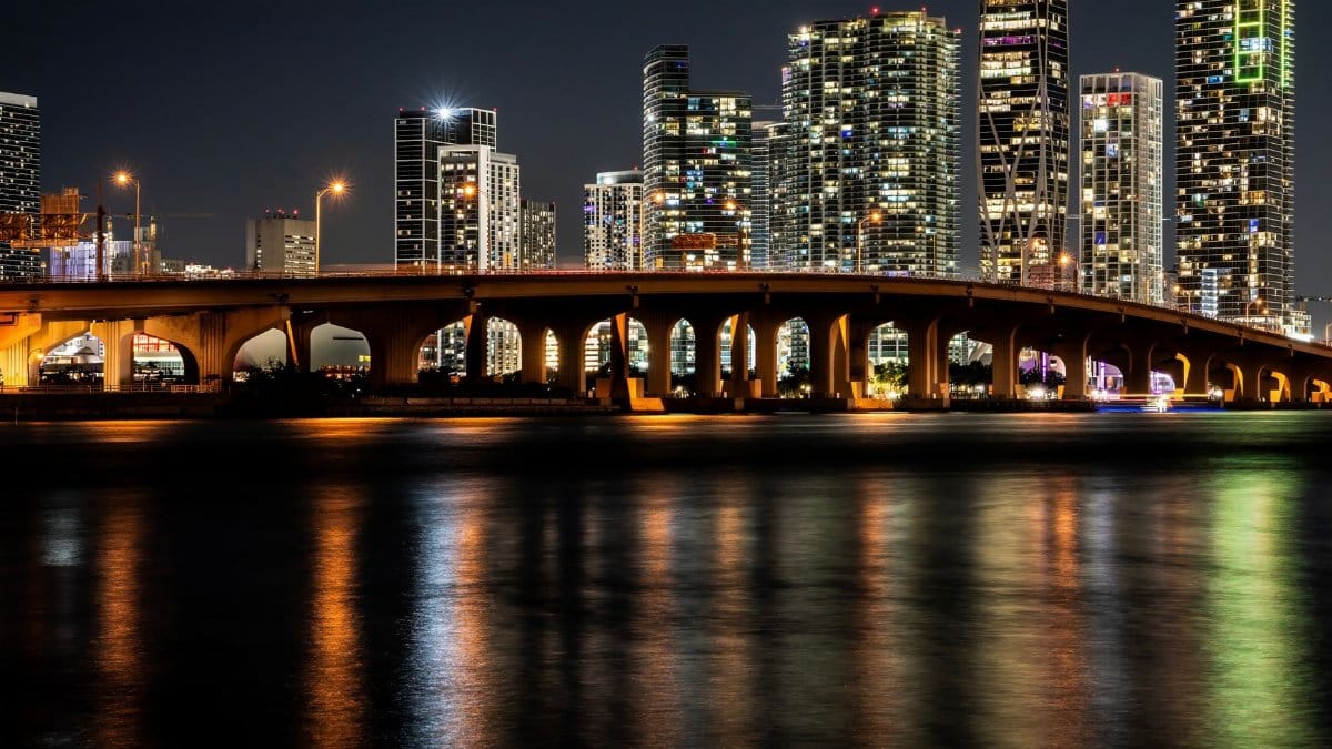 Gorgeous night view of Miami's illuminated skyline and bridge reflections on water, offering a captivating cityscape.