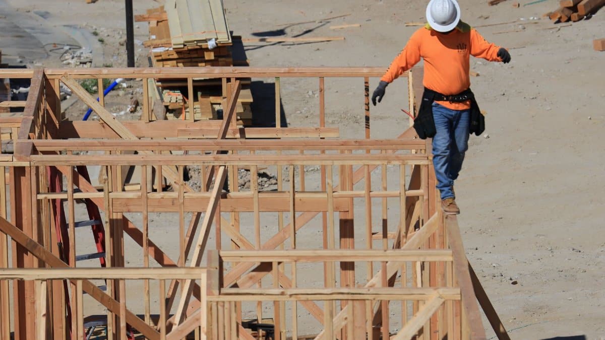 Construction worker balances carefully on a wooden frame at a building site, emphasizing safety and skill.