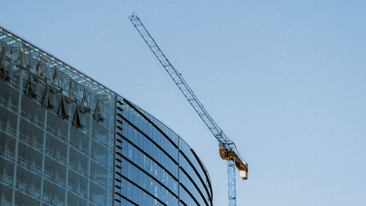 Contemporary glass building under construction with a visible crane against a clear blue sky.