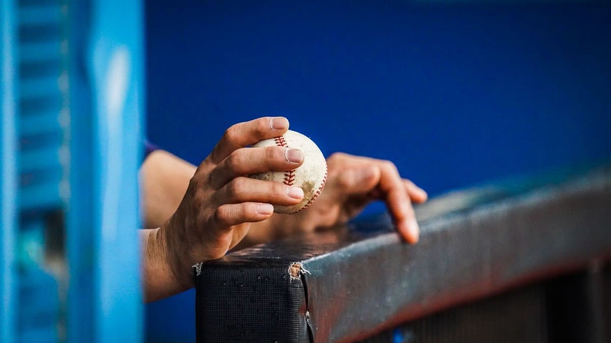 Detailed close-up of a hand holding a baseball over a dugout railing, capturing a moment of anticipation.