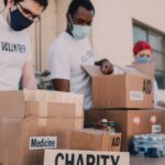 Group of volunteers wearing masks organizing donation boxes labeled food and medicine outdoors.