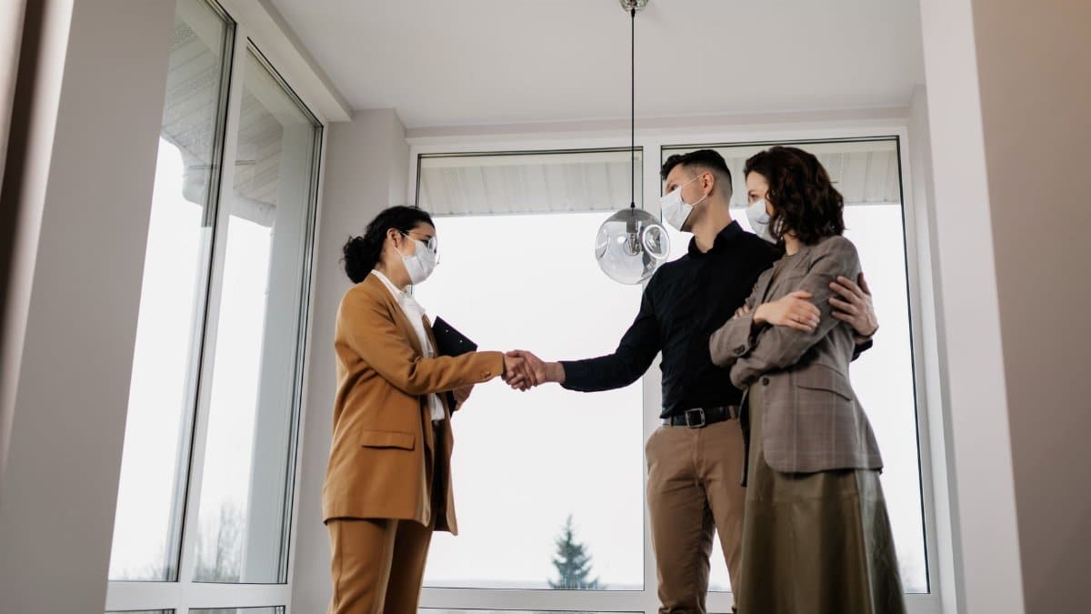 Real estate agent closing deal with couple indoors, all wearing face masks for safety.