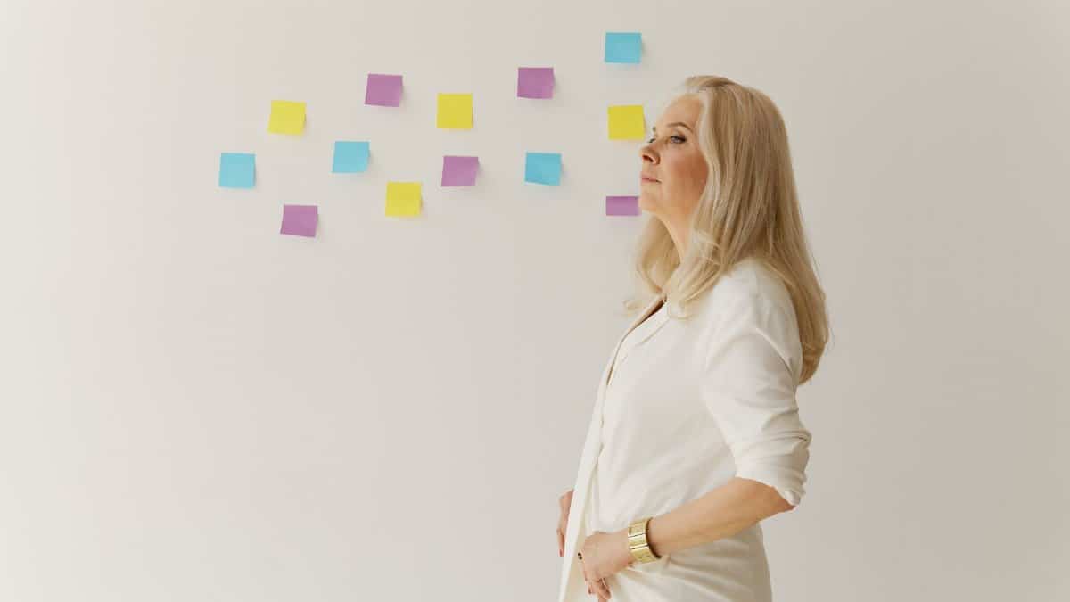 Confident woman in business attire planning with colorful sticky notes on a neutral background.