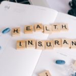 Scrabble tiles spelling 'Health Insurance' on planner with pills and laptop, symbolizing healthcare planning.