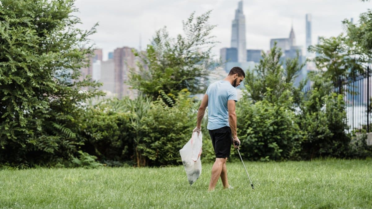 Man picking up litter in a park with the city skyline in the background, promoting environmental conservation.
