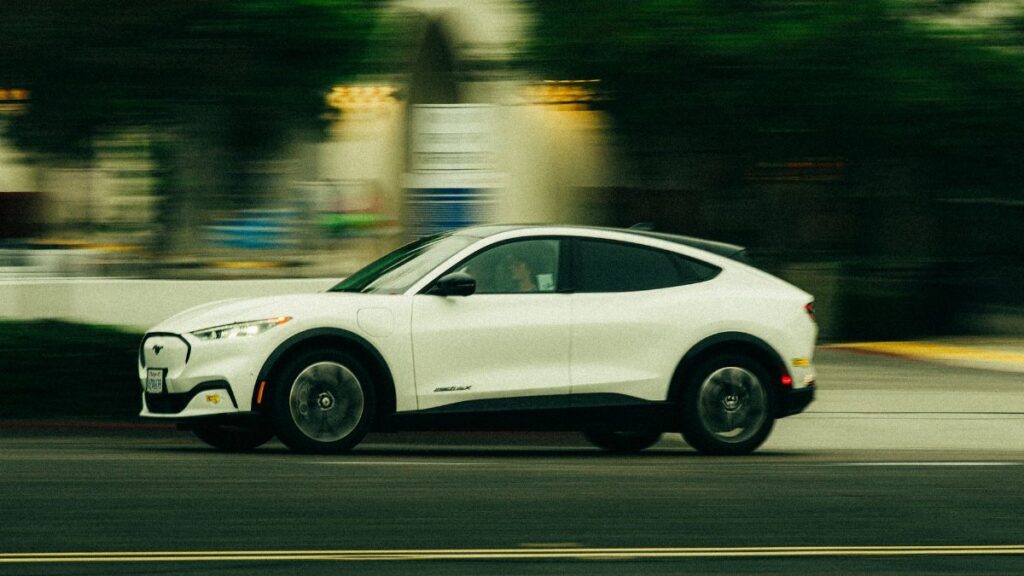 A white electric vehicle speeds through the streets of San Diego, California, showcasing modern automobile design.