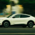 A white electric vehicle speeds through the streets of San Diego, California, showcasing modern automobile design.