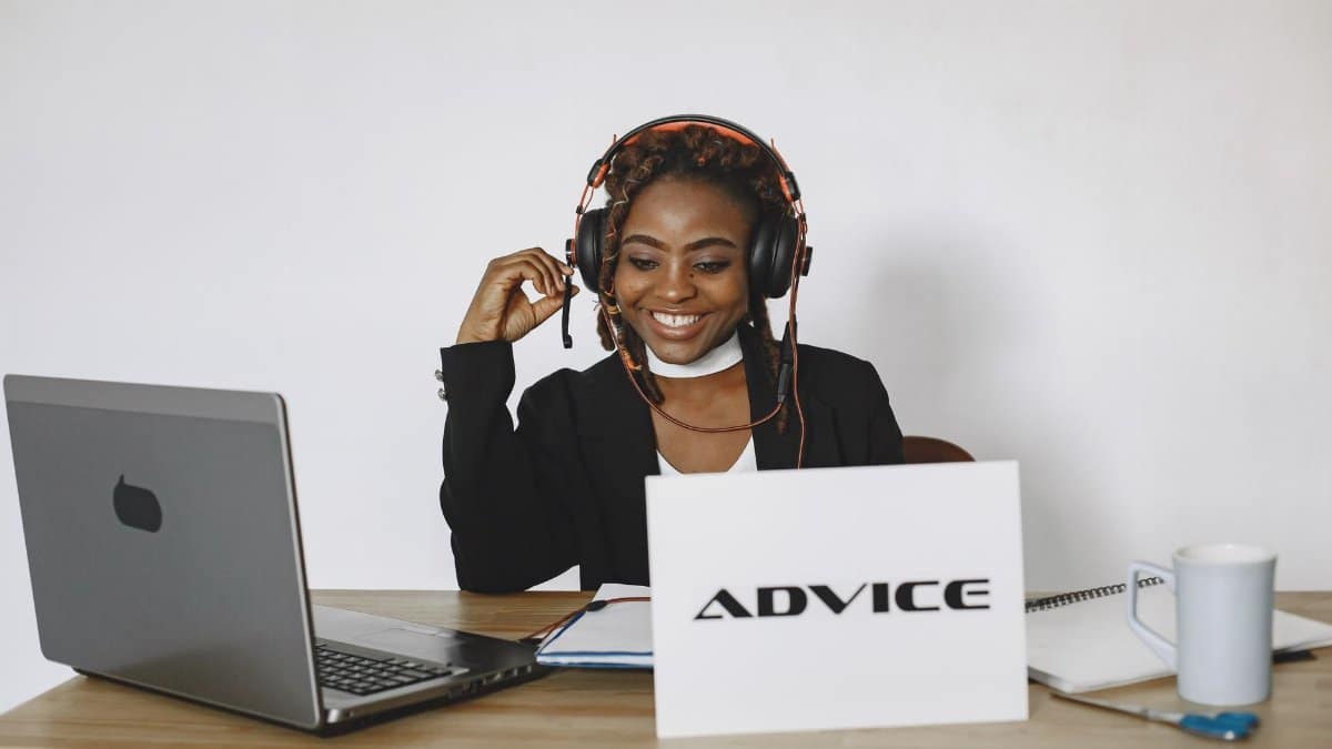 An African American woman smiling while providing online advice using a laptop and headphones.