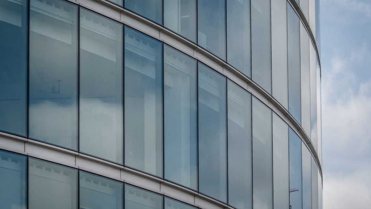 Curved glass facade of a modern office building in Greater London with blue sky reflections.