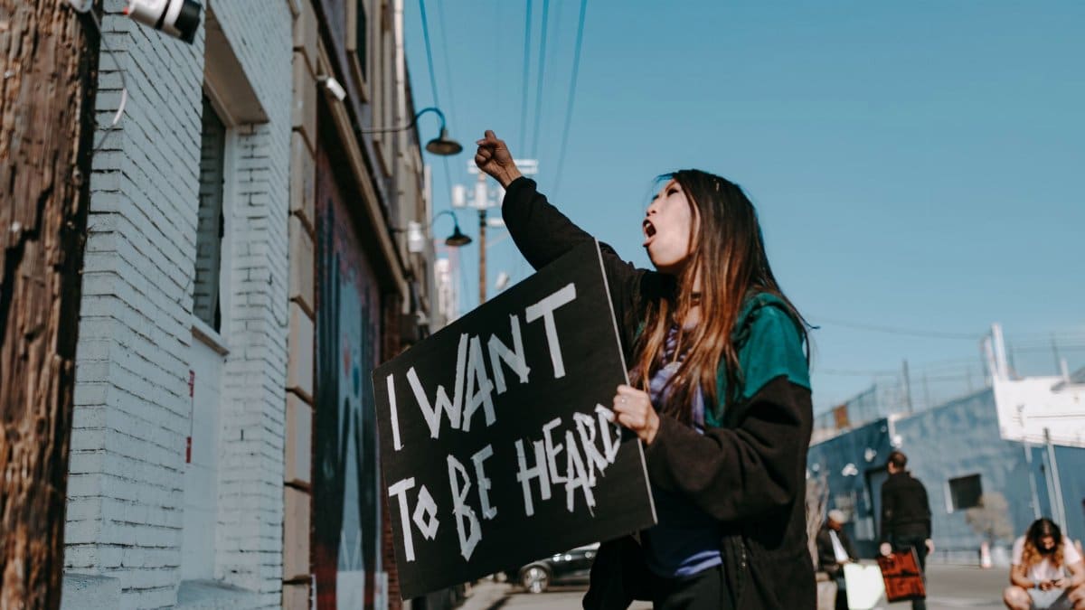 A young woman passionately protests on the street holding a sign.