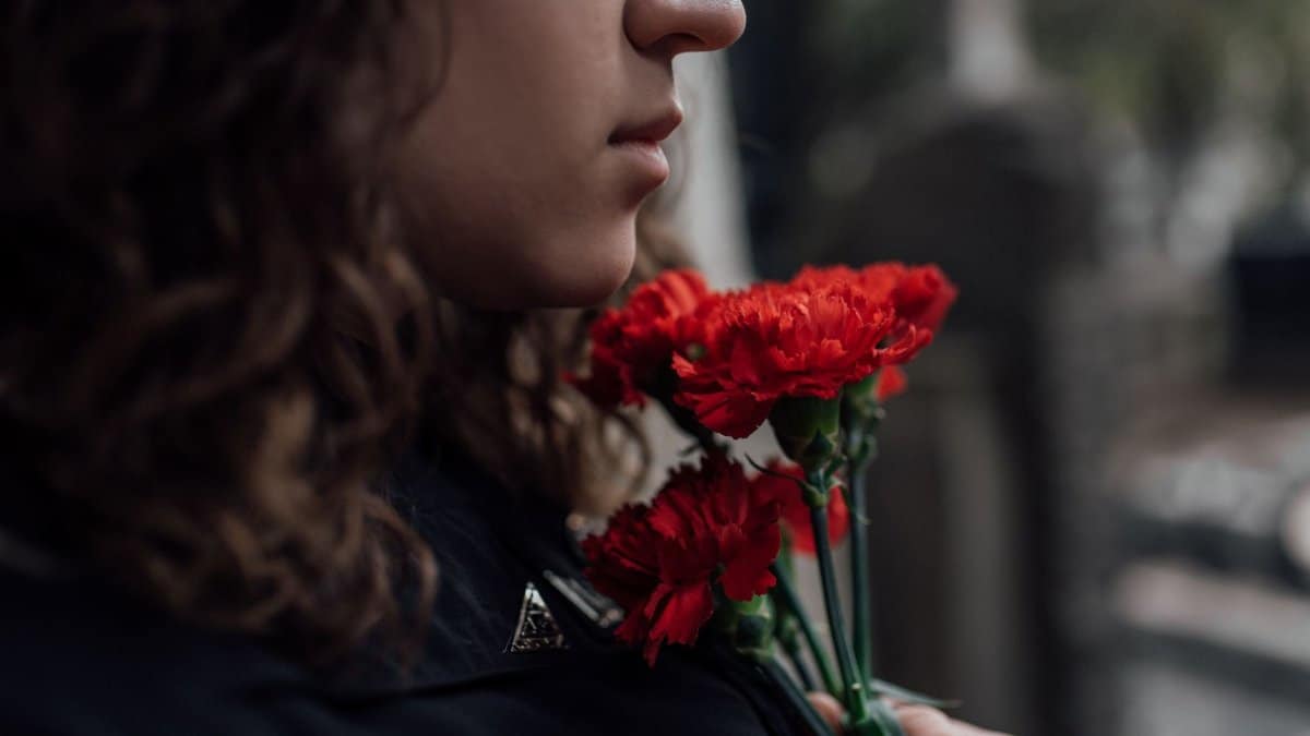 Side profile of a woman holding red carnations, symbolizing grief and loss.