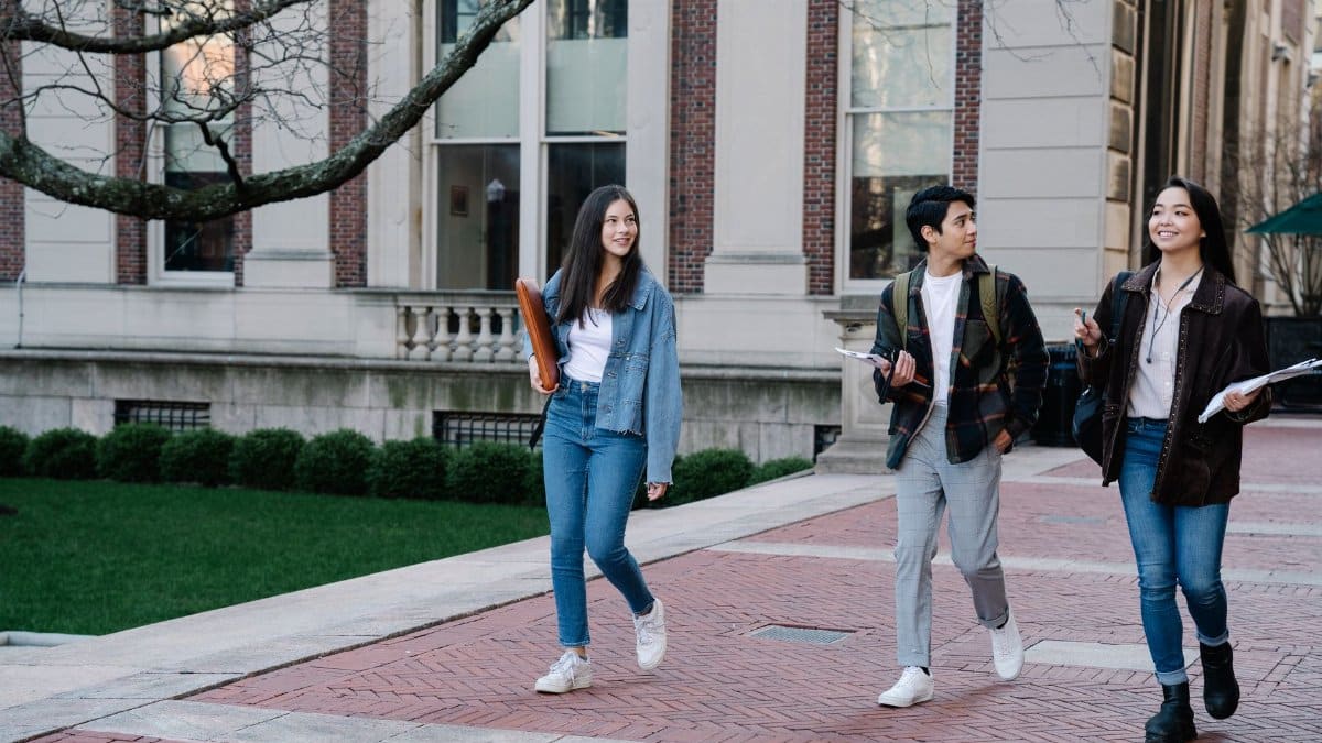Group of young students walking on campus sidewalk on a bright day, showcasing casual university life.