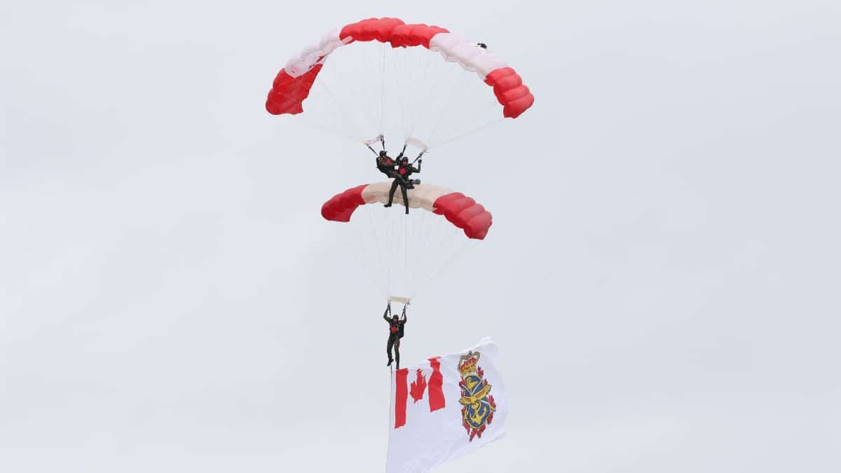 Two skydivers perform a tandem jump displaying a Canadian flag against a cloudy sky.