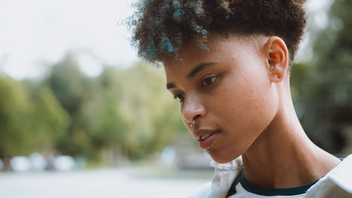 Close-up profile portrait of a stylish young person with colorful hair outdoors.