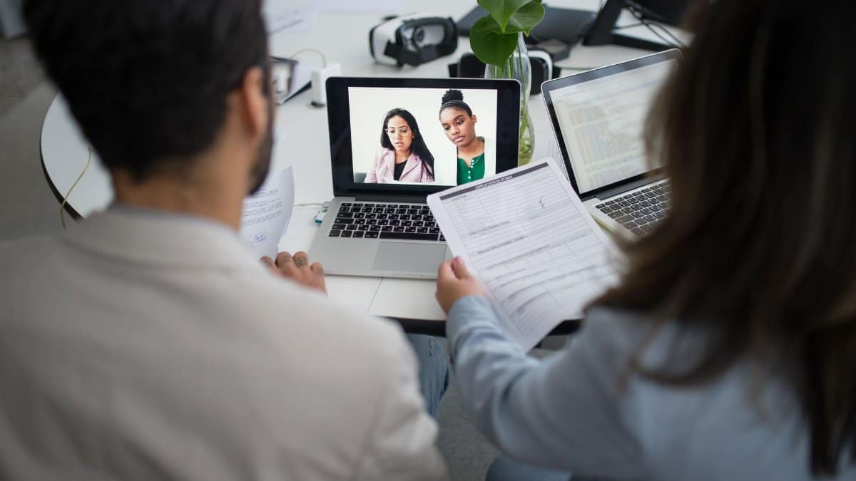 Two professionals conduct a virtual job interview using laptops in a modern office.