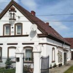 Scenic view of a classic Polish home with white facade and gable roof, showcasing early 20th-century architecture.