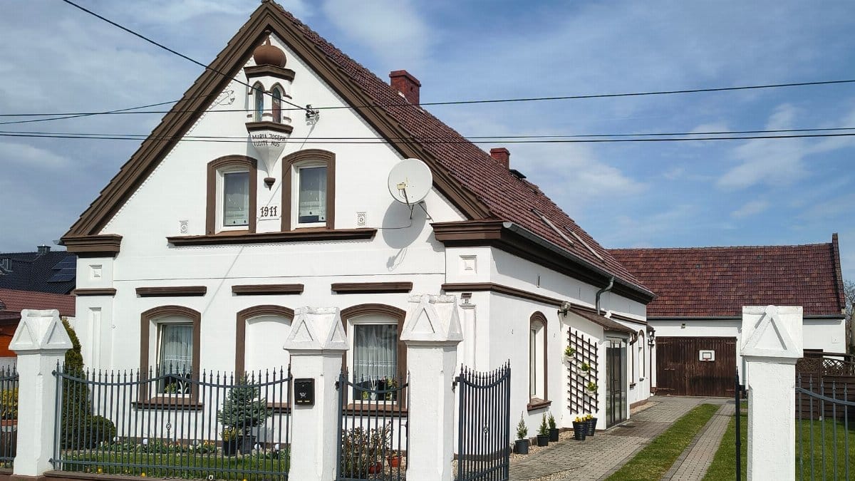 Scenic view of a classic Polish home with white facade and gable roof, showcasing early 20th-century architecture.