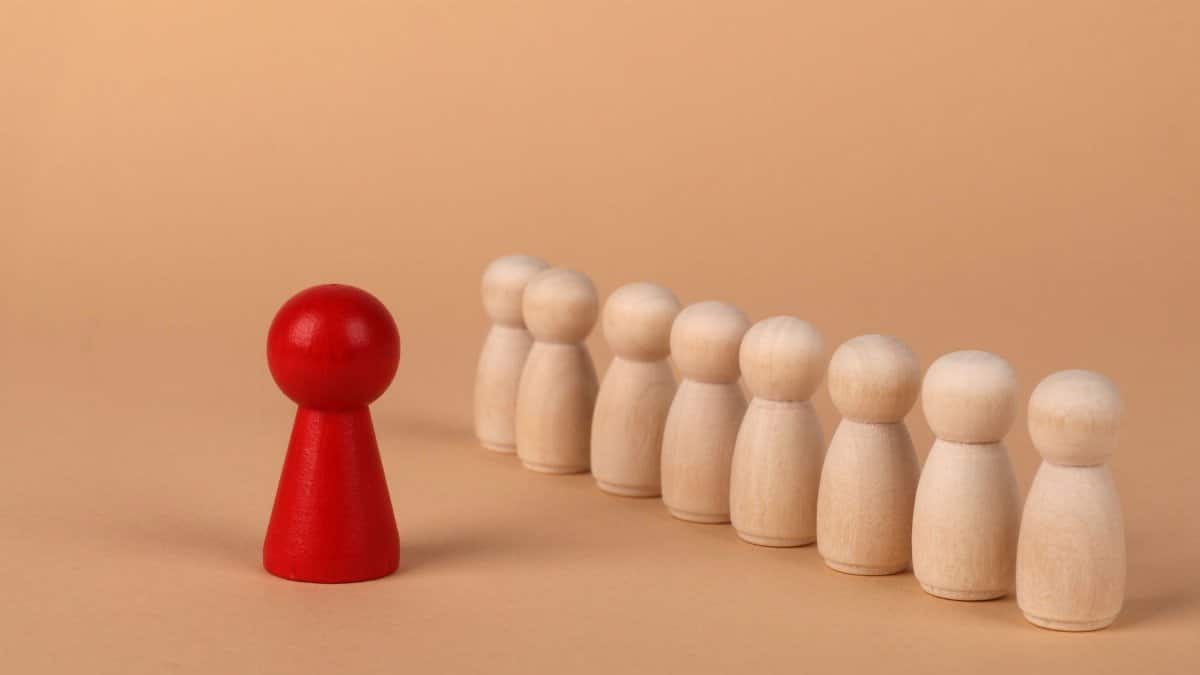 A red pawn stands out as it leads a group of wooden pawns on a beige background symbolizing leadership.