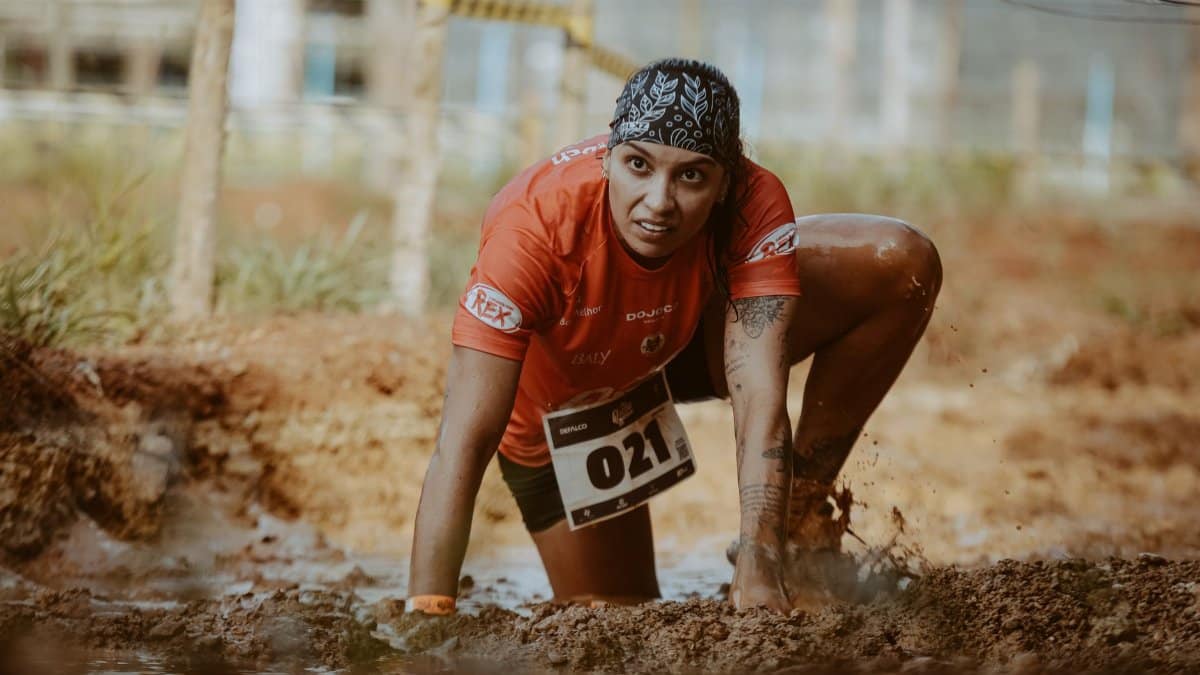 A determined female athlete in a muddy obstacle race, showing grit and focus.