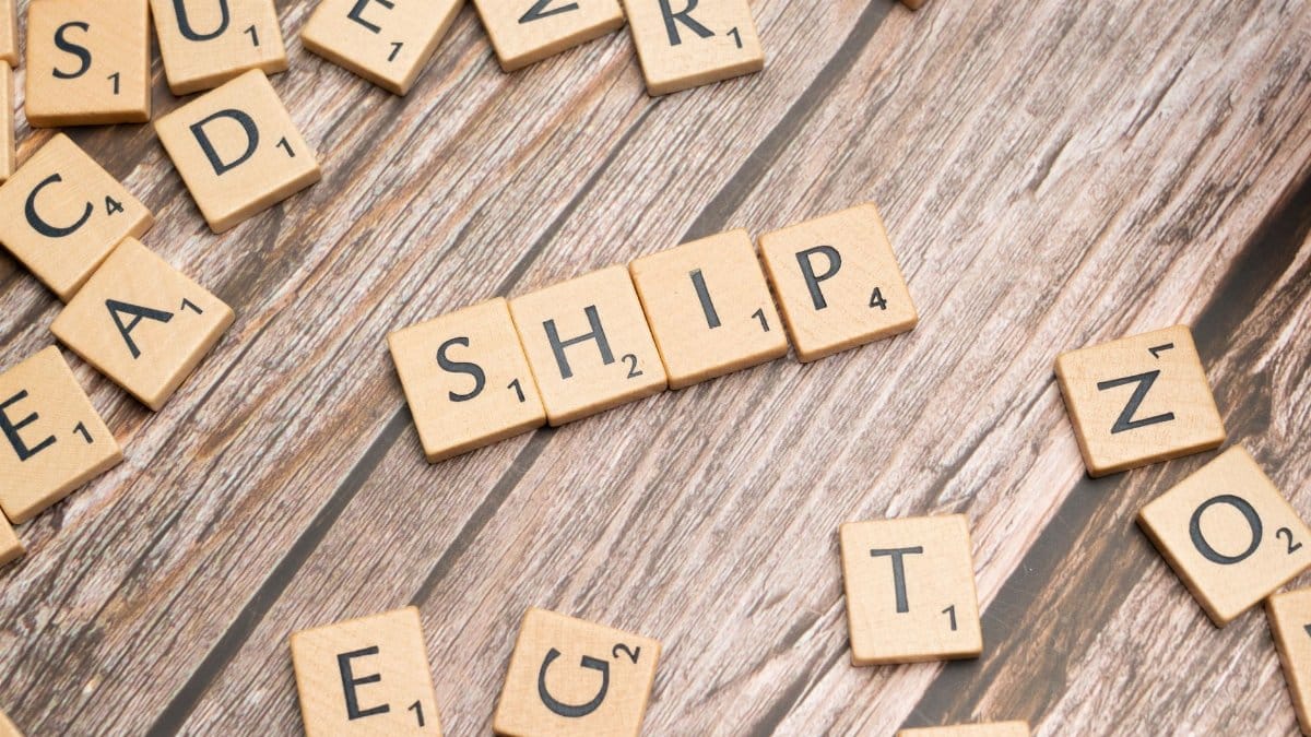 Wooden Scrabble tiles forming the word 'ship' on a rustic wooden surface.