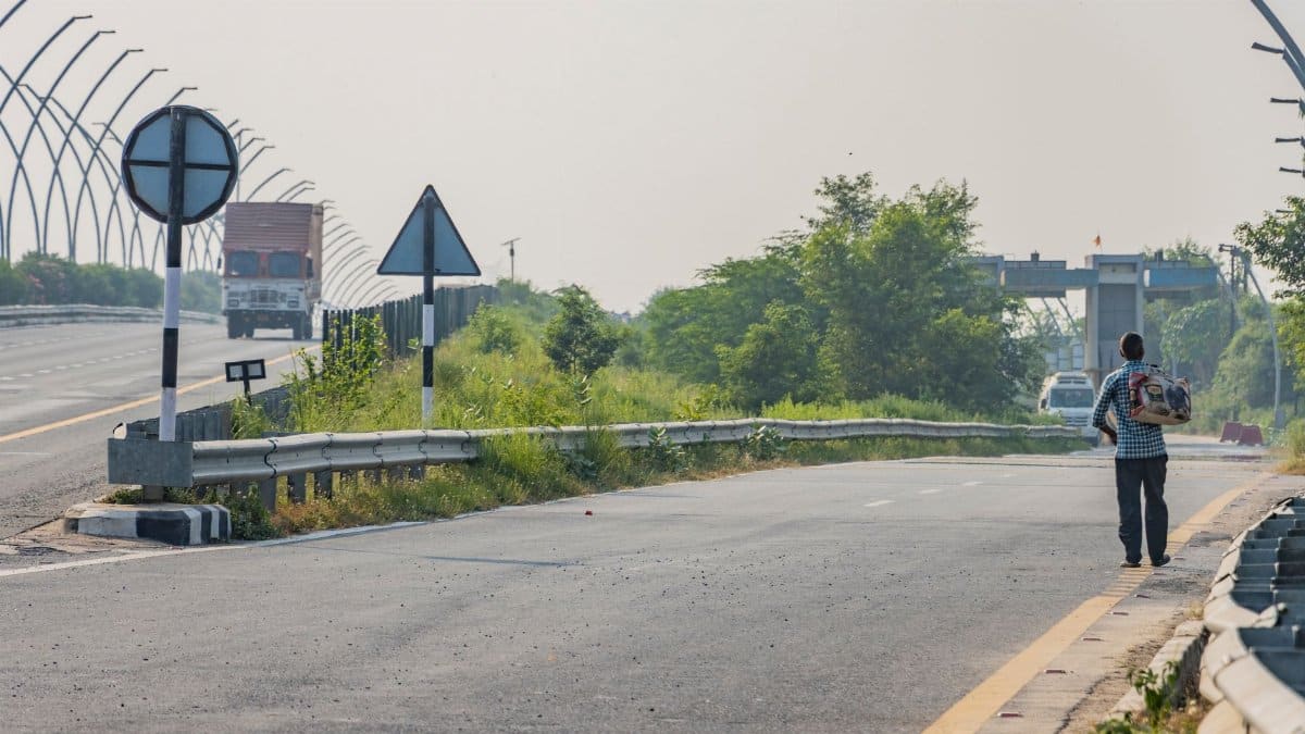A man walks along the highway in Deeg, Uttar Pradesh, India, with vehicles in the distance.