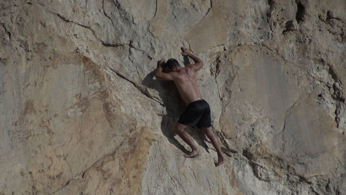 Athletic man engaged in rock climbing on a natural cliff face under sunlight.