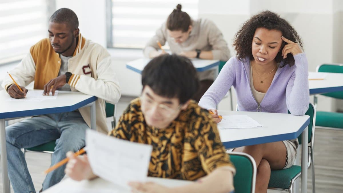 Students of various backgrounds focused on an exam in a bright, modern classroom setting.