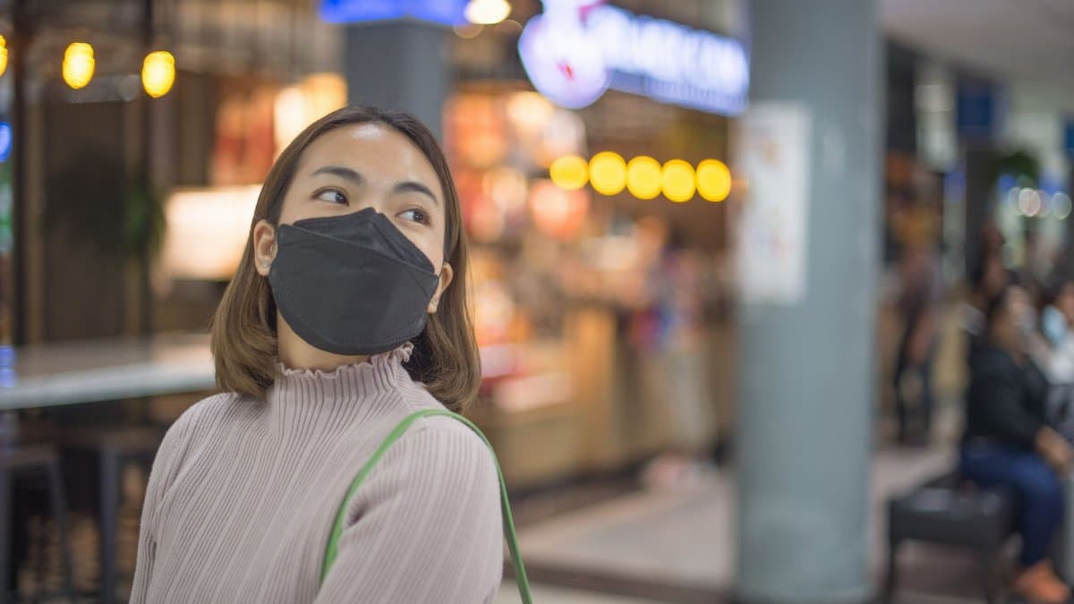 A woman wearing a mask shopping in a bustling Bangkok mall, Thailand.