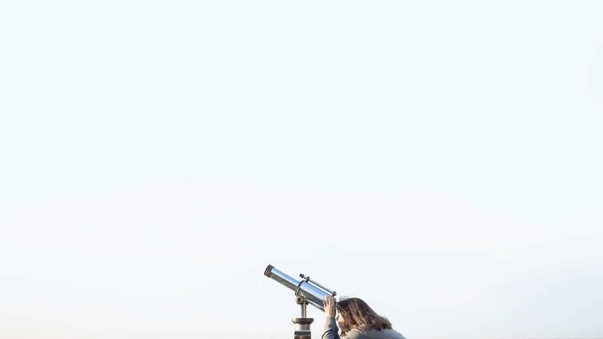 A woman peers through a coin-operated telescope overlooking a city skyline.