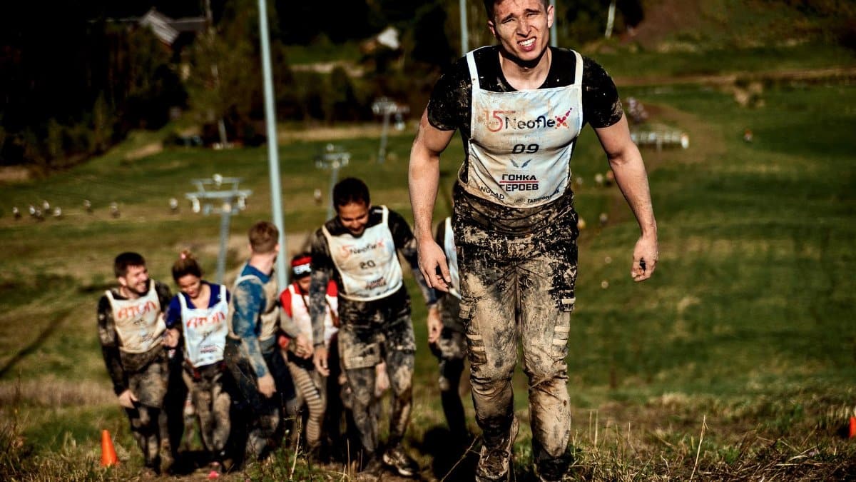 Group of determined competitors battling a muddy hill during an outdoor obstacle race.