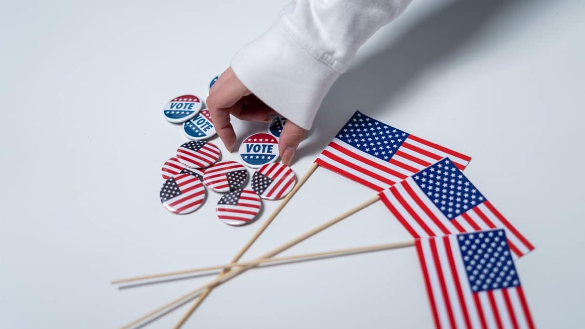Hand reaching for voting buttons and USA flags, symbolizing patriotism and democratic duty.