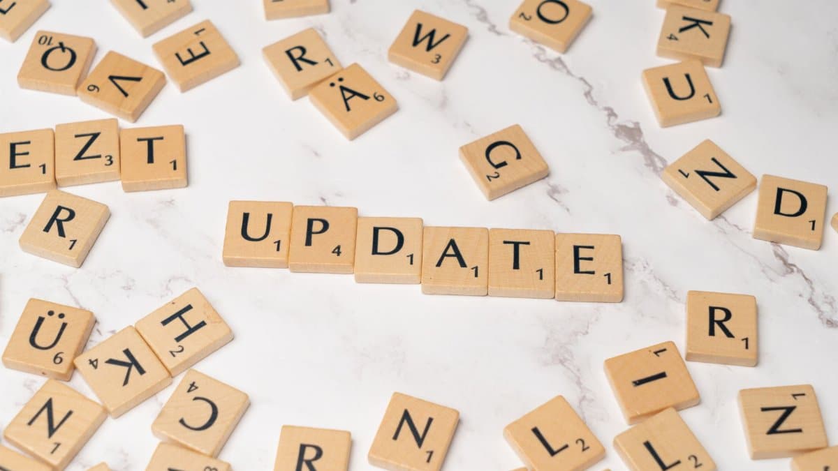 Wooden Scrabble tiles arranged to spell 'Update' among scattered letters on a marble background.