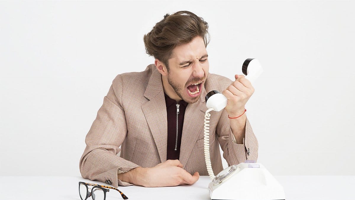 Businessman in a beige suit shouting into a vintage telephone, expressing frustration at work.