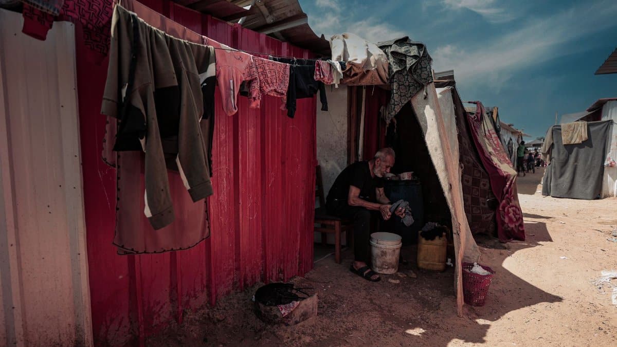 A man sitting outside a makeshift shelter in Gaza, daily life in a refugee camp.