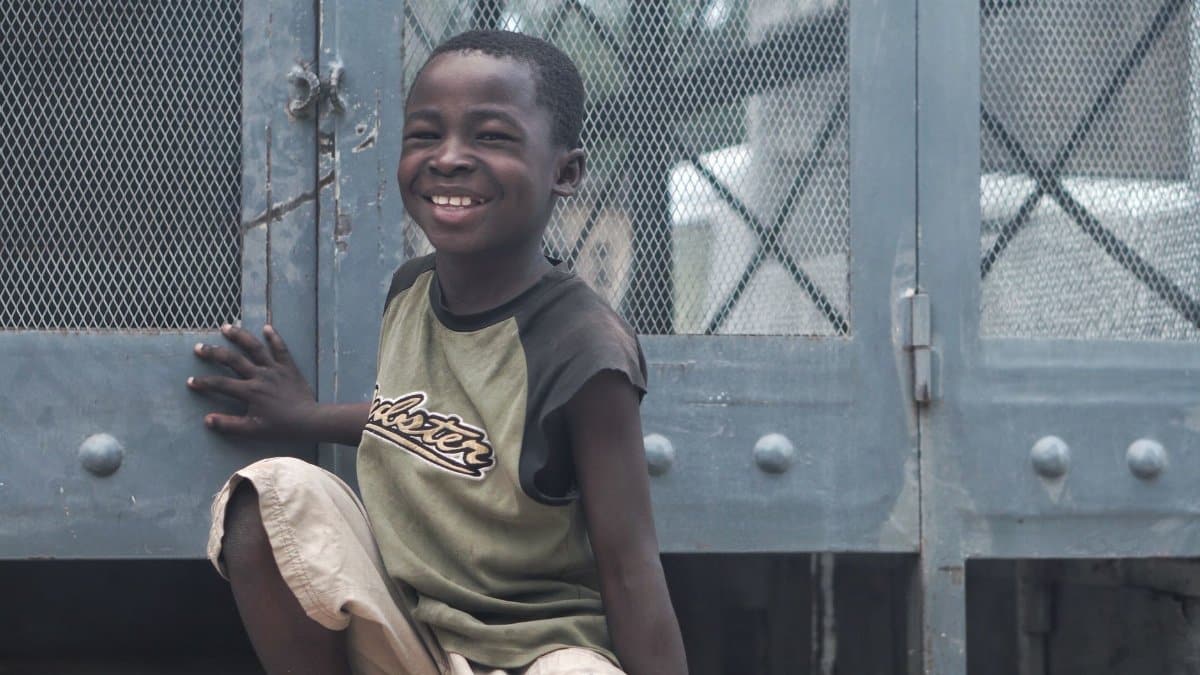 Happy child in Haiti smiles brightly while sitting outdoors.