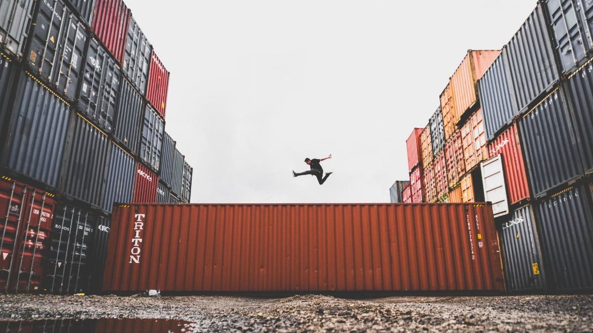 A person leaps dramatically above stacked shipping containers, showcasing freedom and industrial energy.