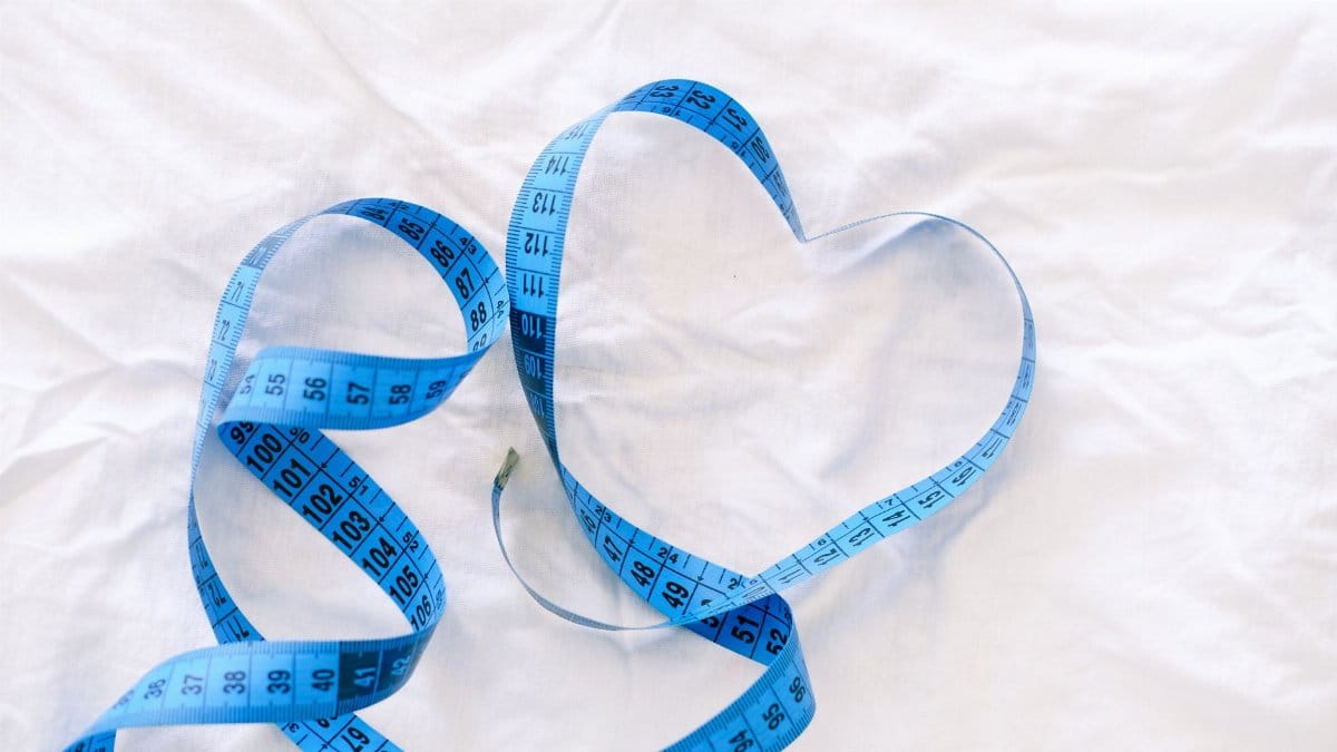 Blue measuring tape forming a heart on white fabric, symbolizing love and measurements.